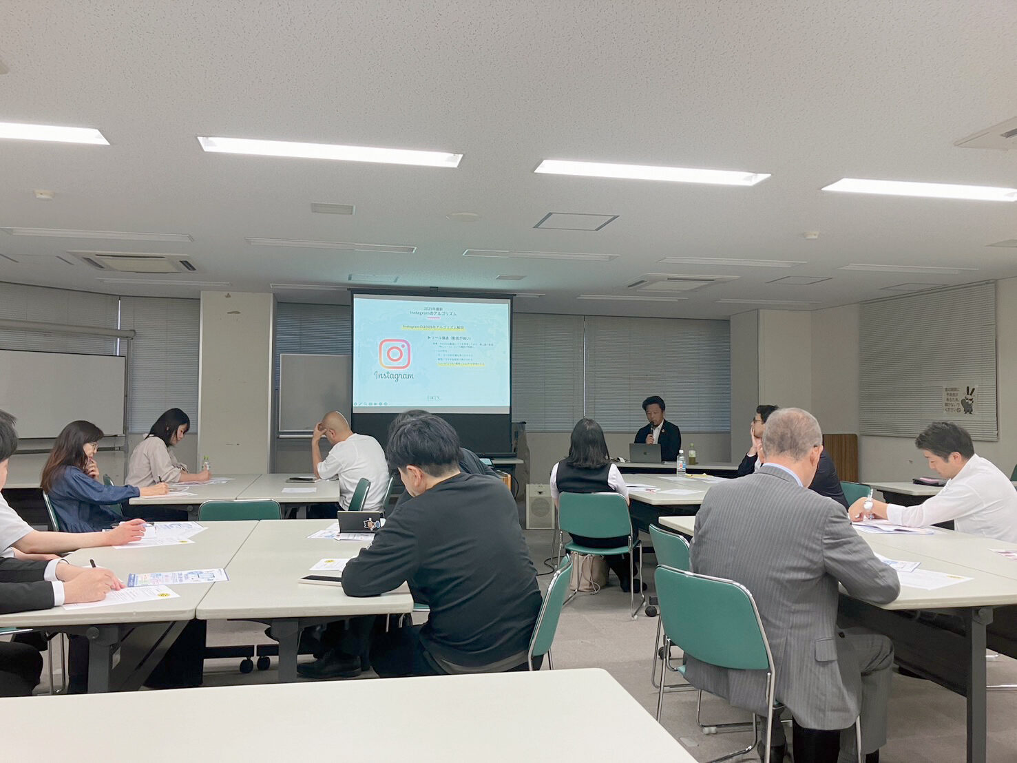 明るい会議室で、投影された資料を見ながら机を囲む研究グループの様子